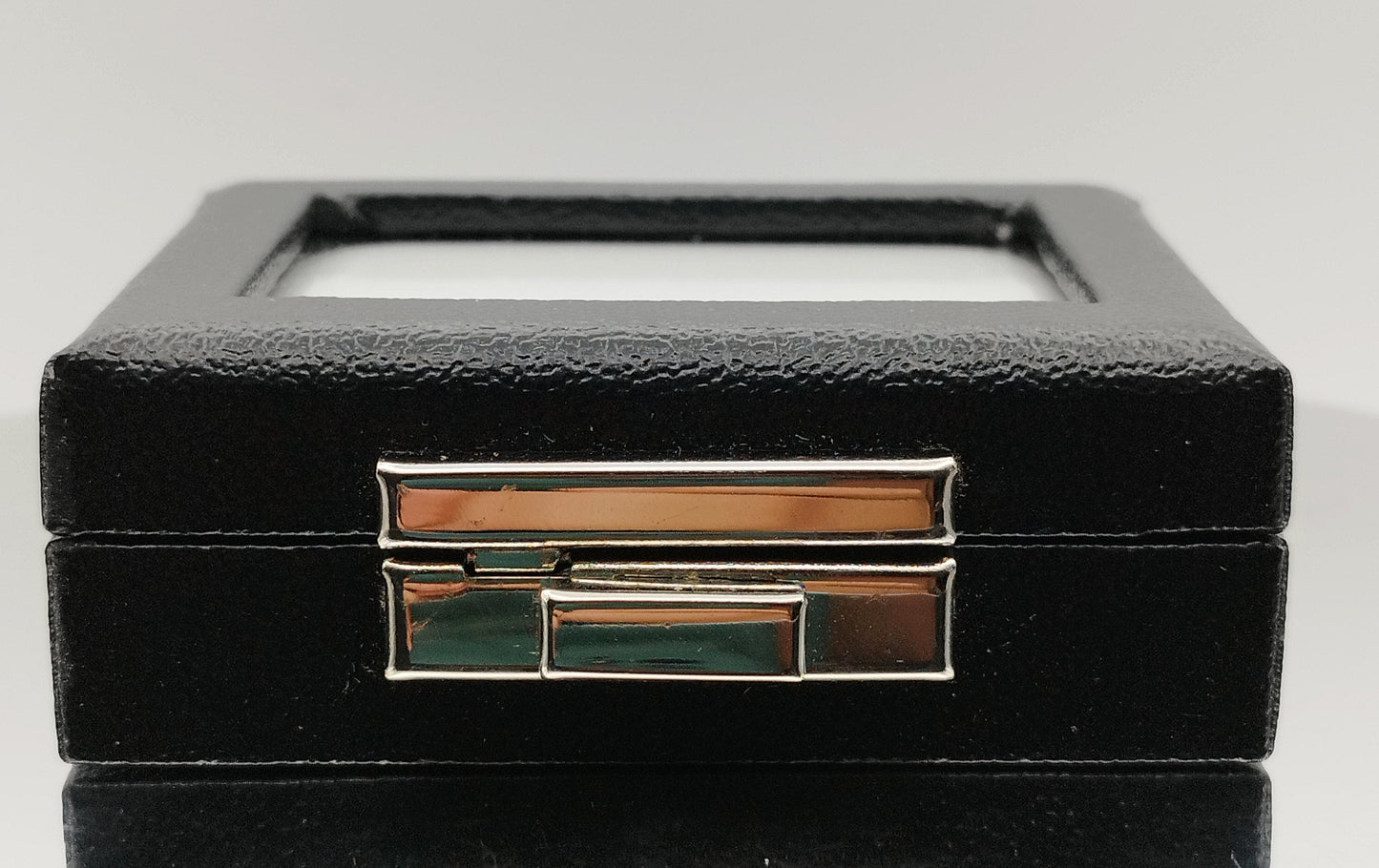 Leather-like black box with metal clasp, transparent top window, and white padded cushion. (7,5 * 6 * 2,5 cm)